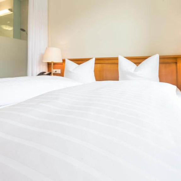 Zwei weiße Kissen und zwei weiße Bettdecken liegen auf einem Doppelbett im Dreibettzimmer
